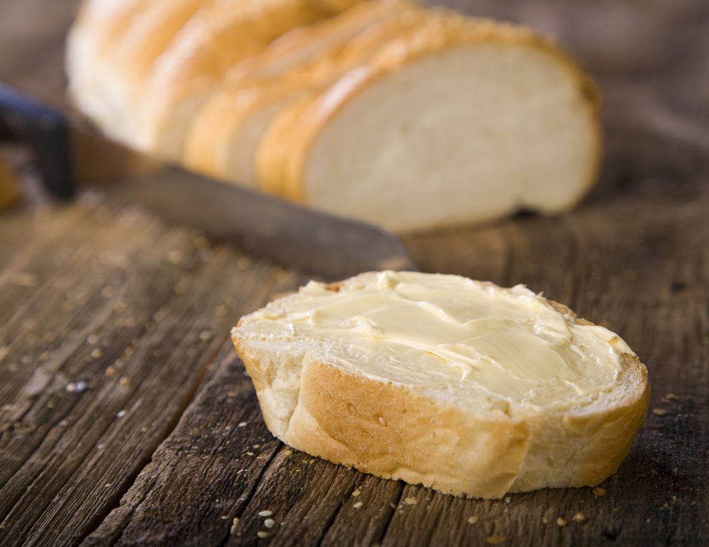 A slice of French bread on a rustic wooden counter.